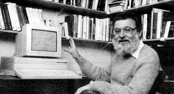 Donald Norman en su despacho durante la década de 1980, posando junto a un ordenador Apple, rodeado de estanterías repletas de libros